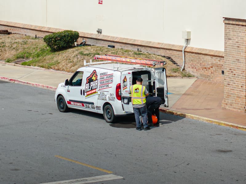 Alpha Electrical work van with a ladder on top parked outside a retail store, two workers at its open rear doors