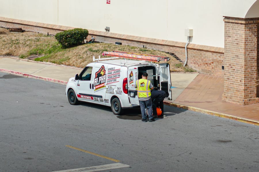 Alpha Electrical work van with a ladder on top parked outside a retail store, two workers at its open rear doors